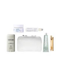 A curated travel self-care gift set arranged on a white background, including a Margin deodorant stick, a white travel cream jar, a clear roll-on bottle, a white zip pouch, a green Davids toothpaste tube, two bamboo toothbrushes, and a small white bottle.
